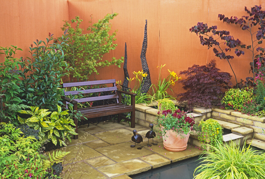 Water feature in orange walled garden with wooden bench