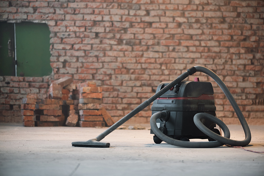 Industrial vacuum hoover in room with tiled floor and brick wall